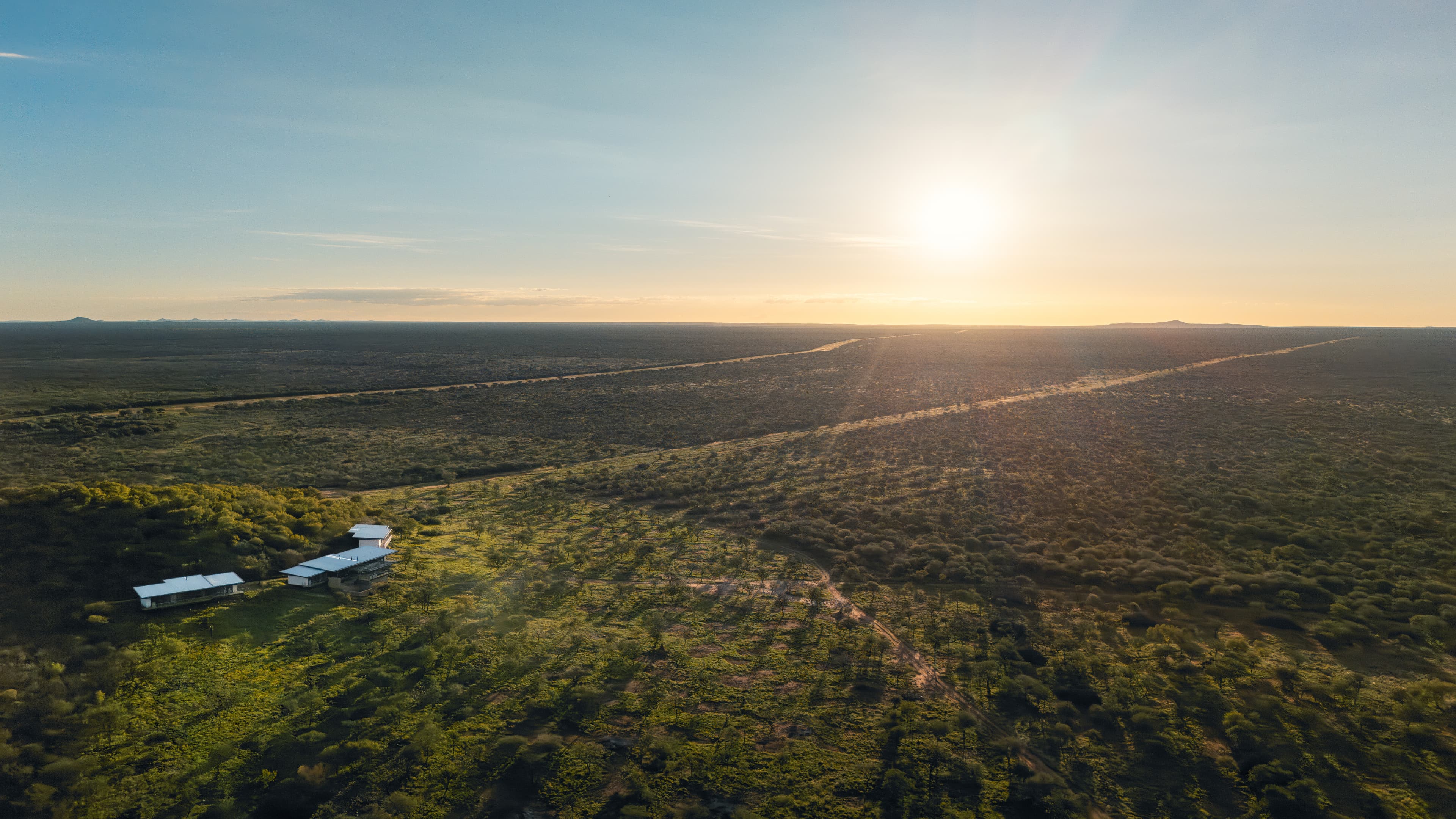Aerial view of modern buildings in a vast savanna landscape during a golden sunset.
