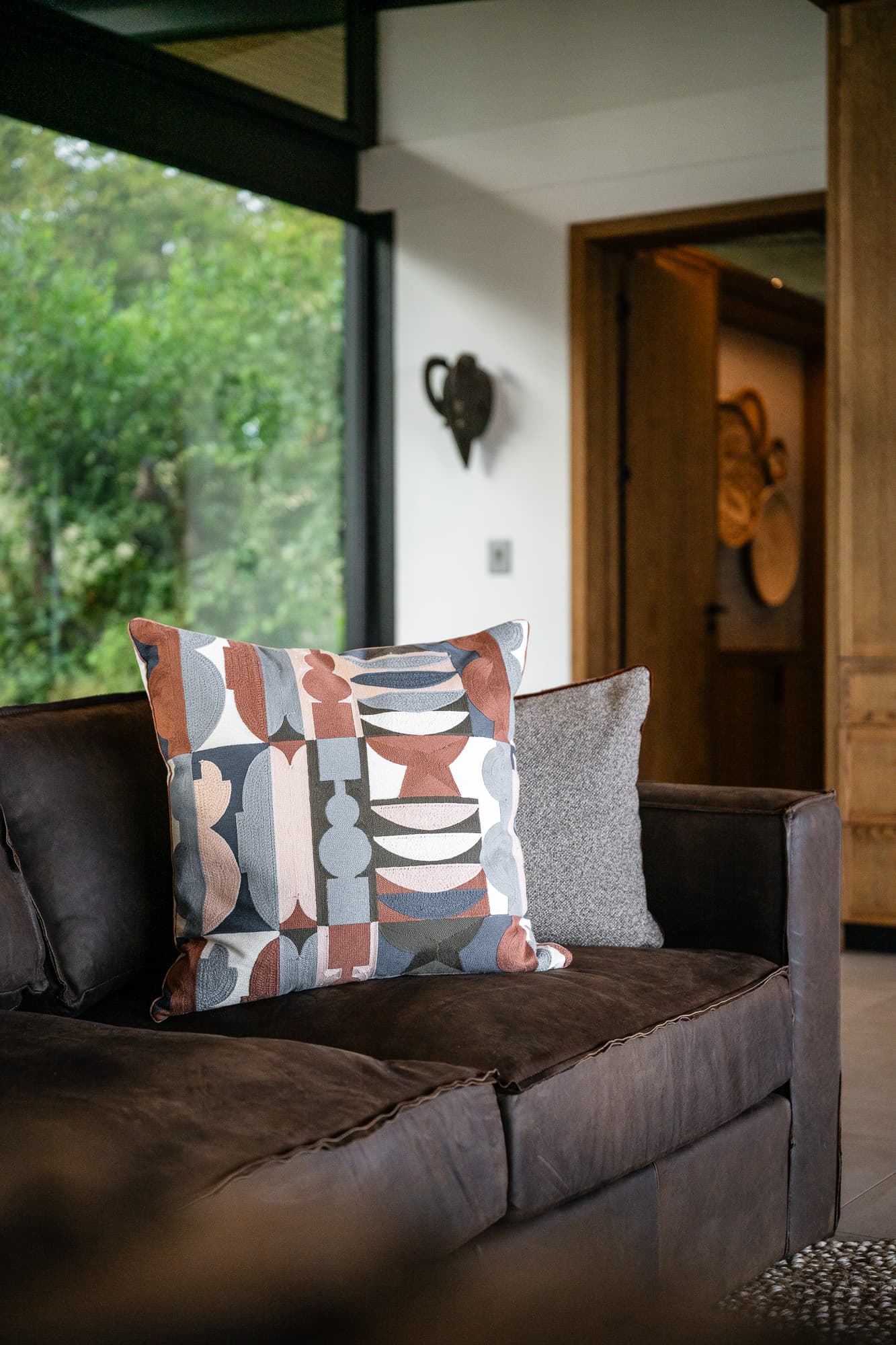 Geometric patterned throw pillow in terracotta and grey on a dark brown leather couch.
